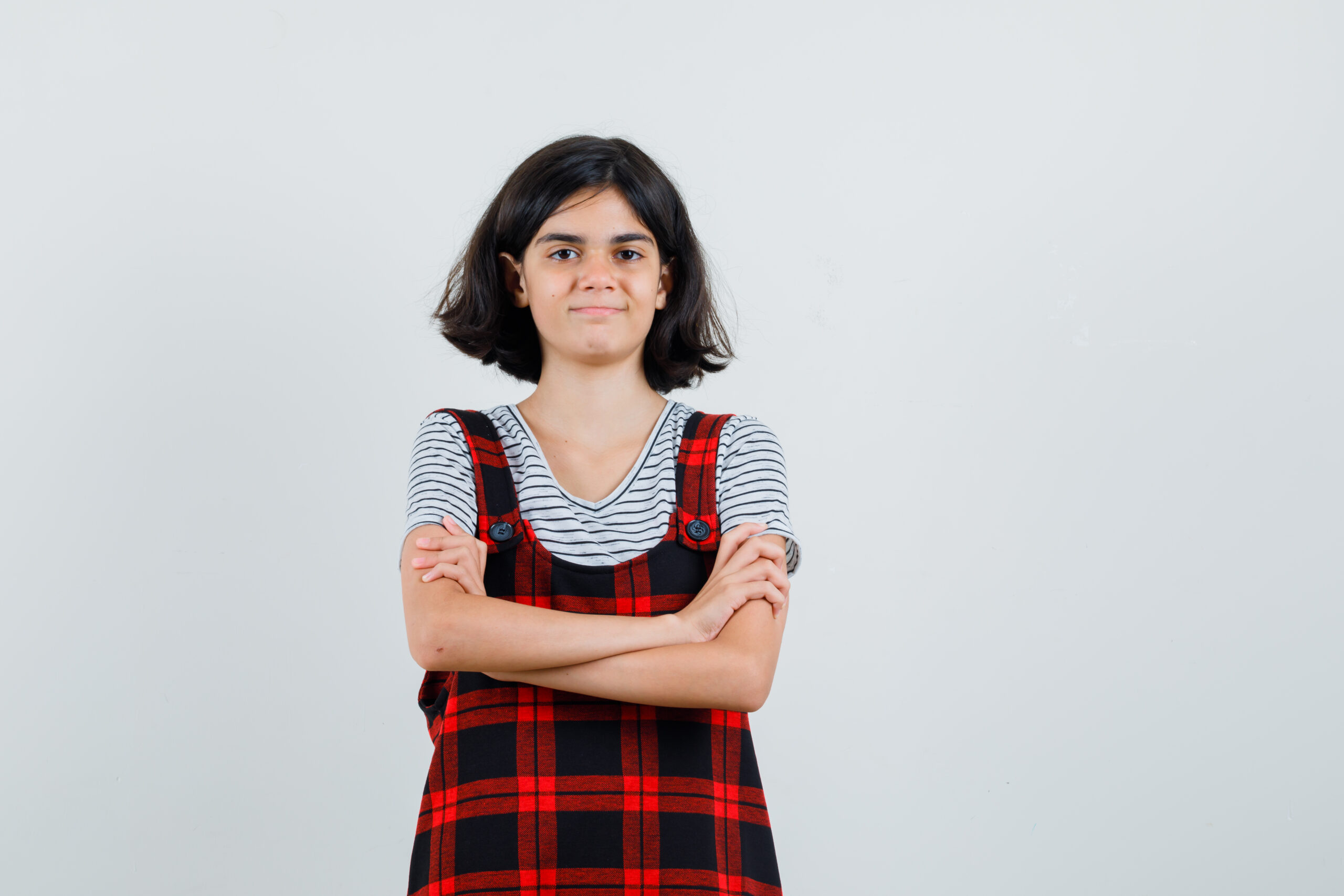 Preteen girl in t-shirt,jumpsuit standing with crossed arms and looking self-confident , front view.